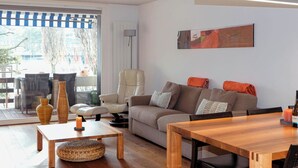 A modern living room with a sofa, a dining table, and a chair. There is a window with a view of the outdoors. - Buchtoase Appartement/Fewo 4-Bett Wohnung by Interhome (Spiez)