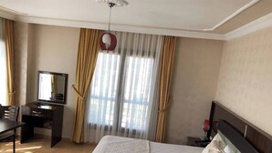 A hotel room with a bed, a desk, a chair, a mirror, and a window with curtains. - YUMURTALIK OTEL (Yumurtalık)