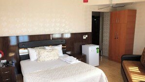 A hotel room with a bed, a desk, a chair, a wardrobe, and a small refrigerator. - YUMURTALIK OTEL (Yumurtalık)