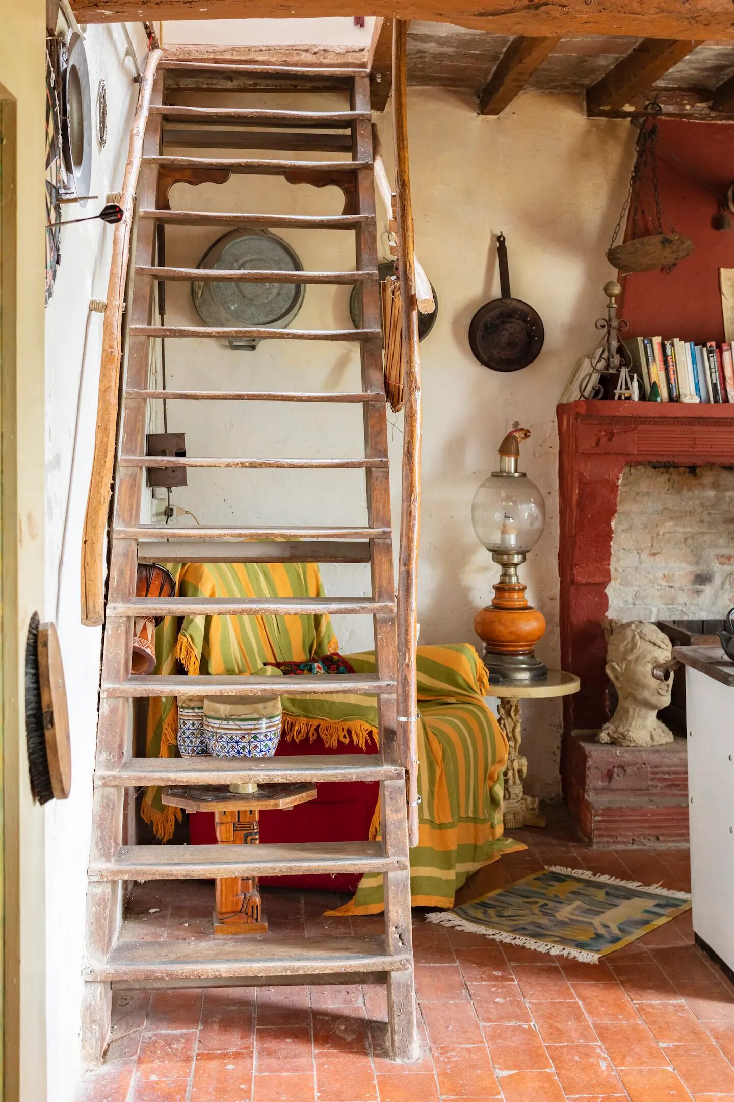 A rustic room with a wooden ladder, a red brick fireplace, a statue, and a shelf with books.