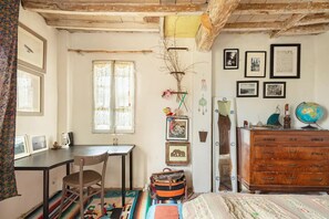 Una habitación con un escritorio de madera, una silla, un aparador y una cama con colcha estampada.