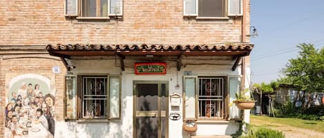 A two-story building with a sign reading 'La Selvatica.' There are two windows with shutters, a door, and a small outdoor seating area with a bench and potted plants.