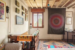 Quarto com cama de madeira, estante, tapeçaria e janela com vista.