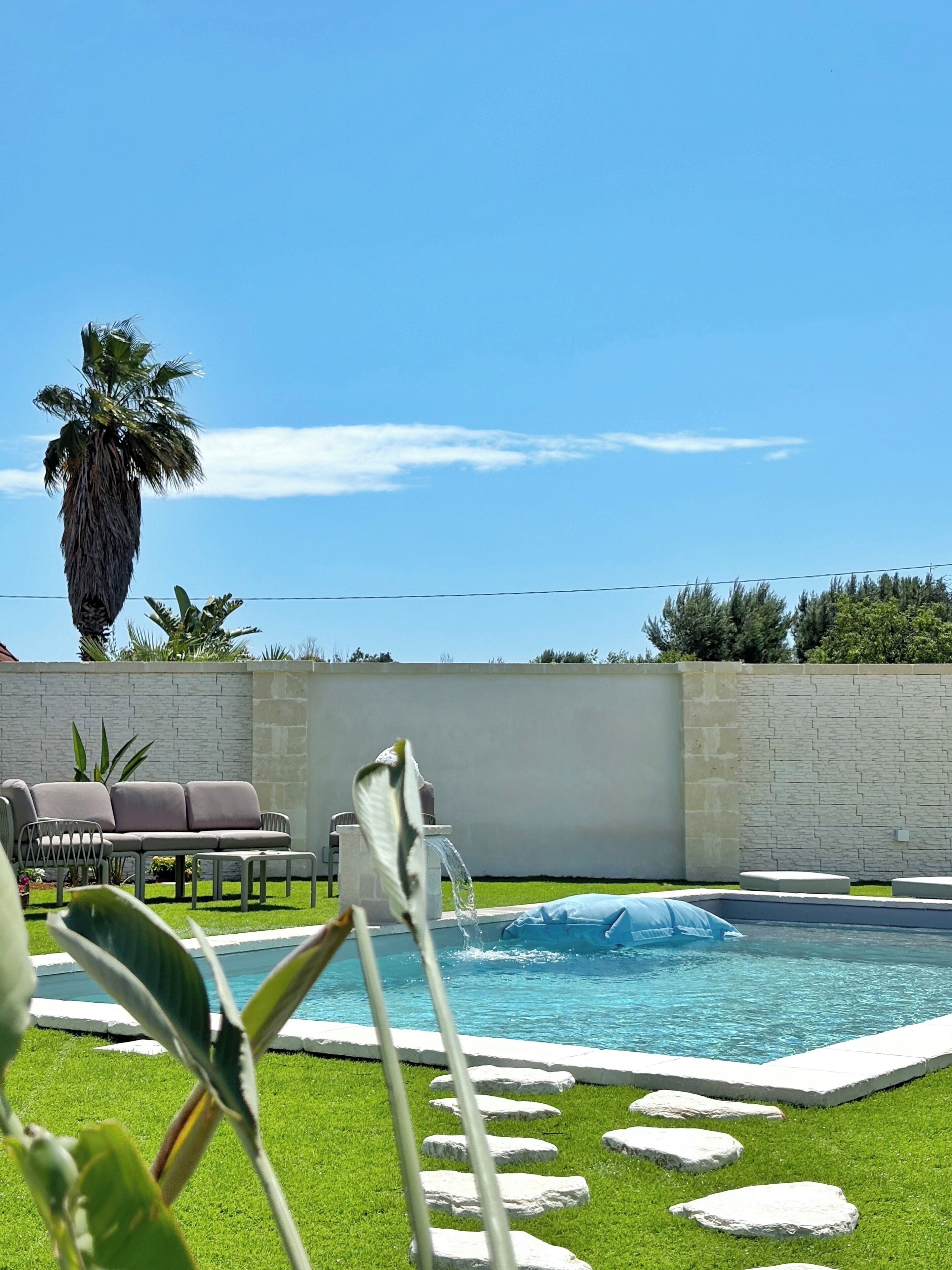 Ein Pool mit Steinrand, einer Palme und einer Steinmauer.