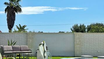 Una piscina con borde de piedra, una palmera y un muro de piedra.