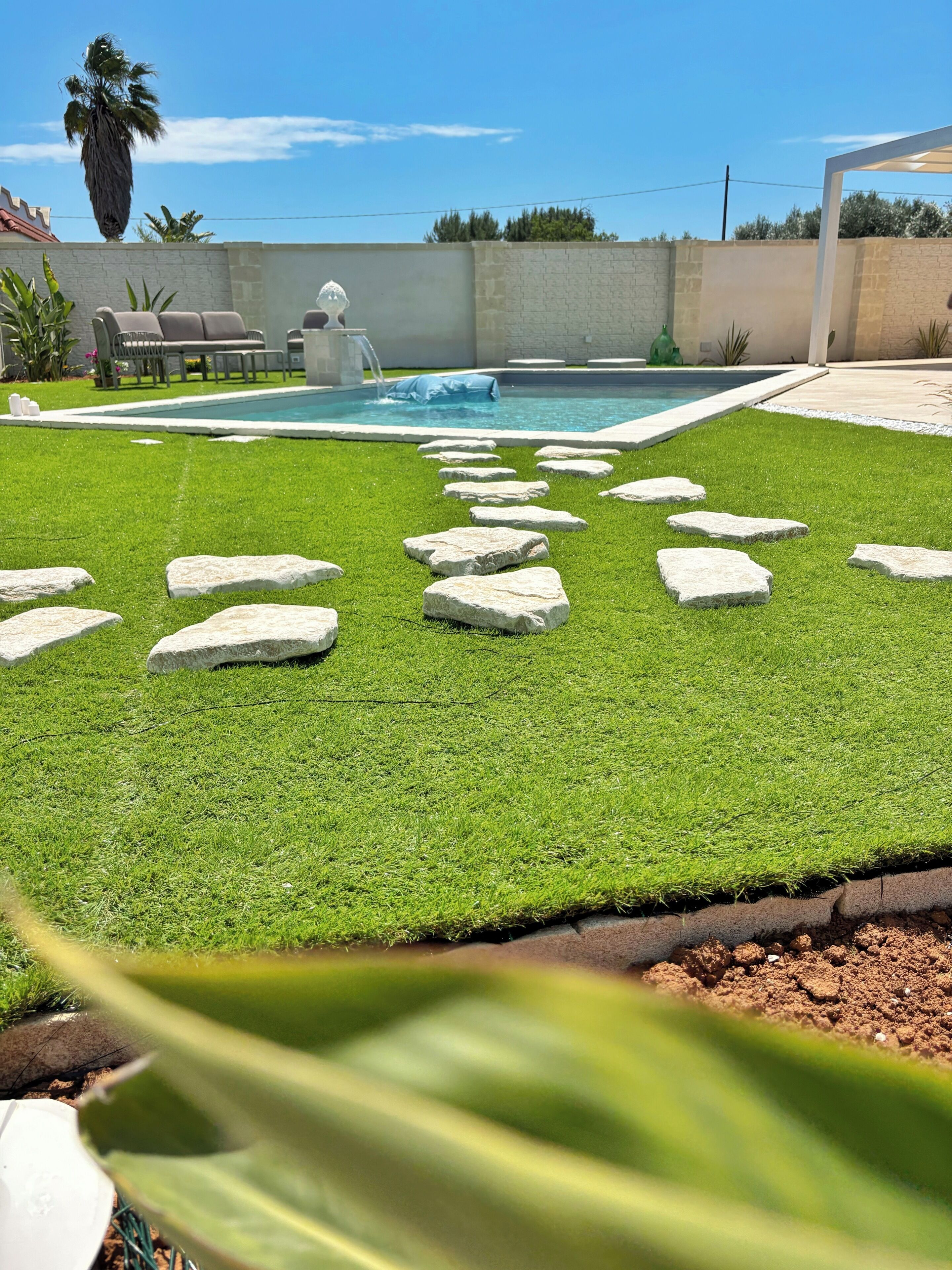 A backyard with artificial grass, a swimming pool, and a stone pathway.