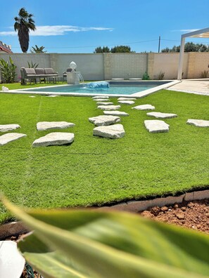 Ein Garten mit Kunstgrashalm, einem Schwimmbad und einem gepflasterten Weg.