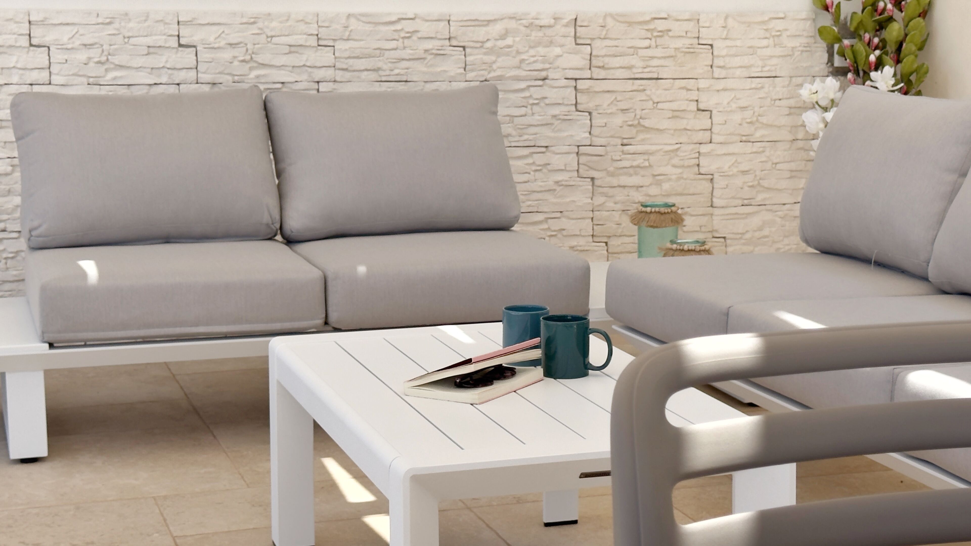 A modern living room with a stone-textured wall, a grey sofa, a white coffee table, and a blue mug.