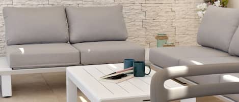 A modern living room with a stone-textured wall, a grey sofa, a white coffee table, and a blue mug.