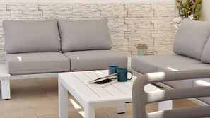 Ein modernes Wohnzimmer mit einer Wand im Steinoptik, einem grauen Sofa, einem weißen Couchtisch und einer blauen Tasse.