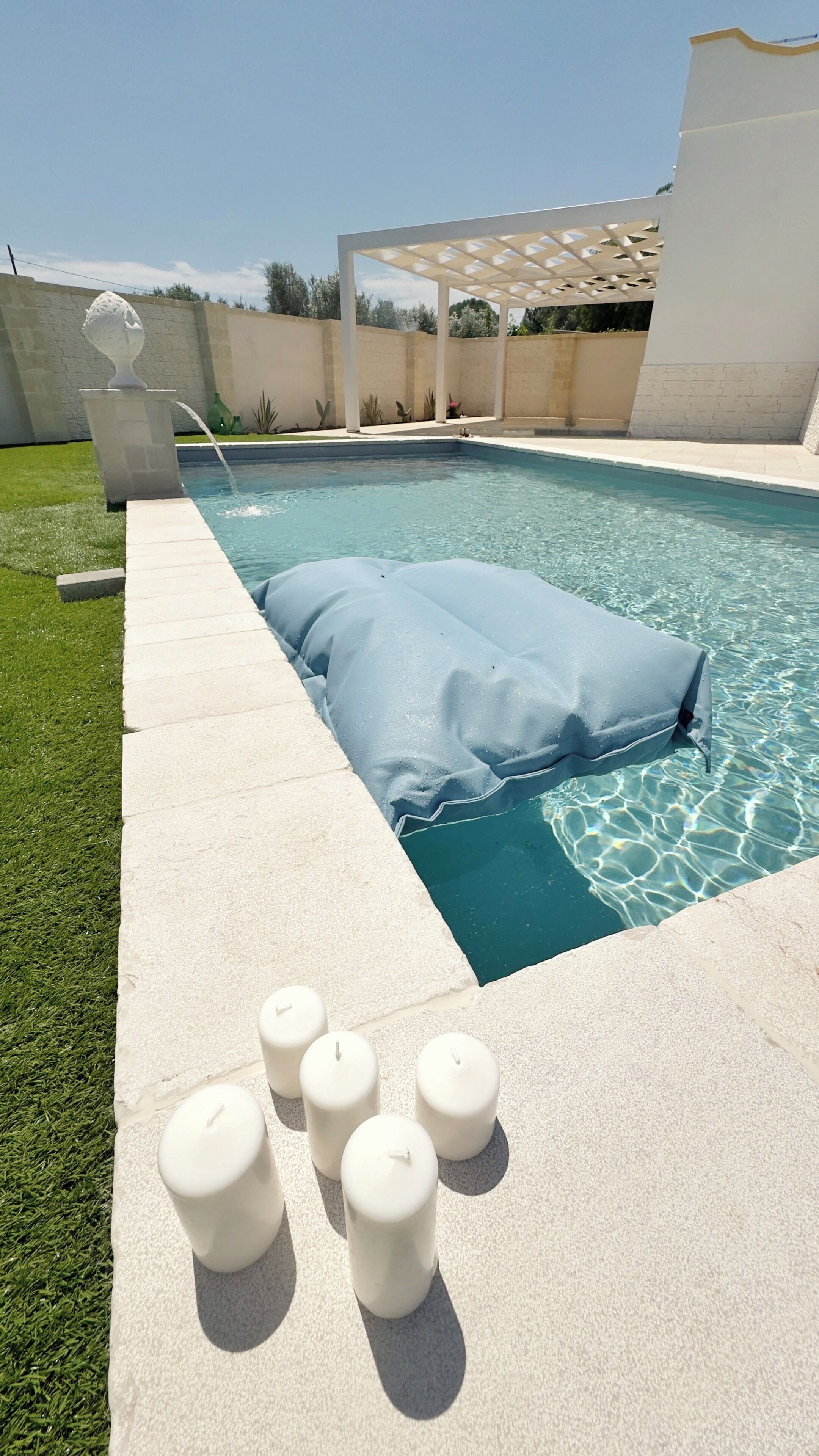 A swimming pool with a covered area, a white wall, and a small garden with plants.