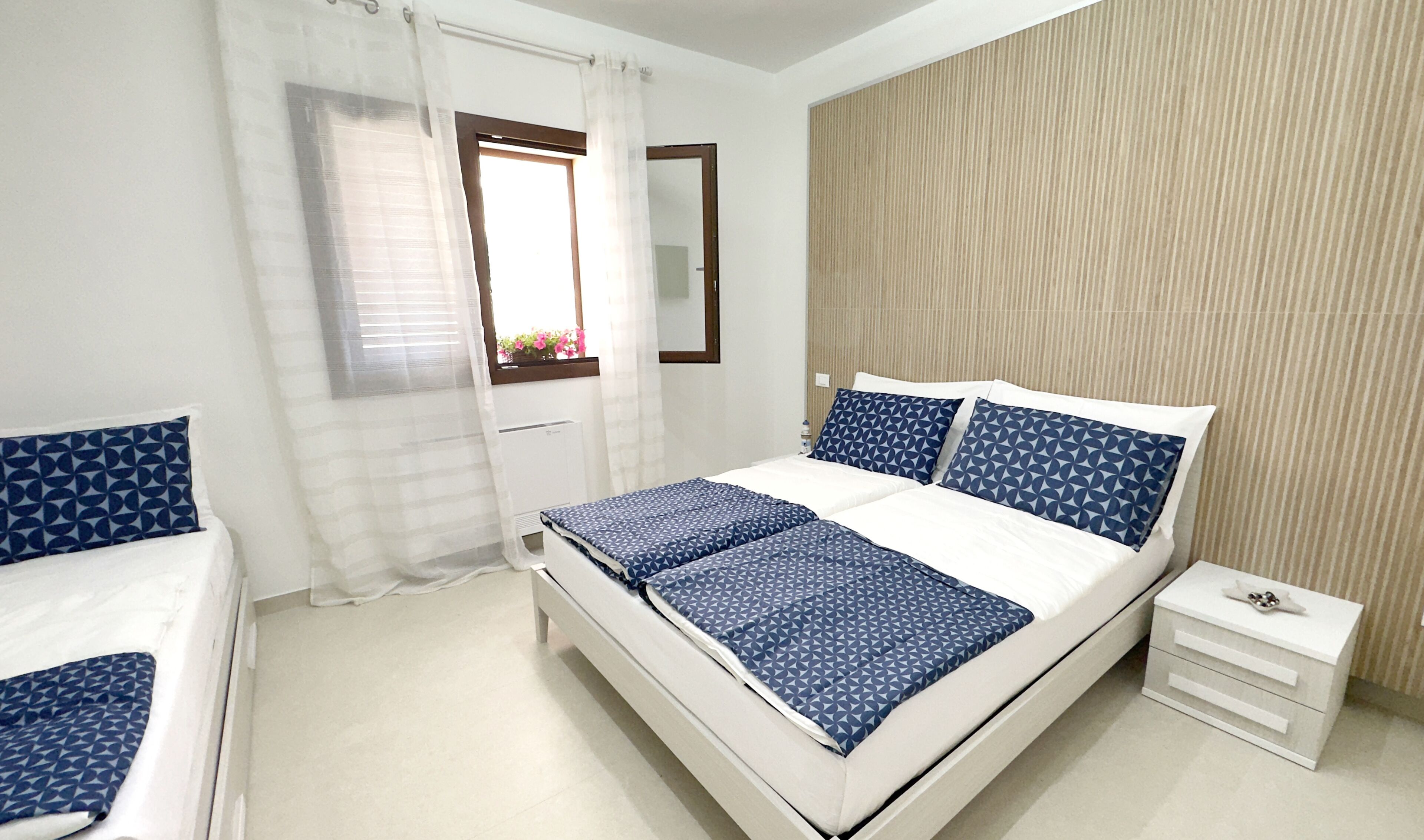 Un dormitorio con cama, mesita de noche, ventana con cortinas y pared con textura.