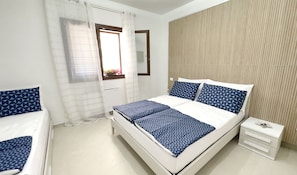 Ein Schlafzimmer mit Bett, Nachttisch, einem Fenster mit Vorhängen und einer Wand mit strukturierter Oberfläche.