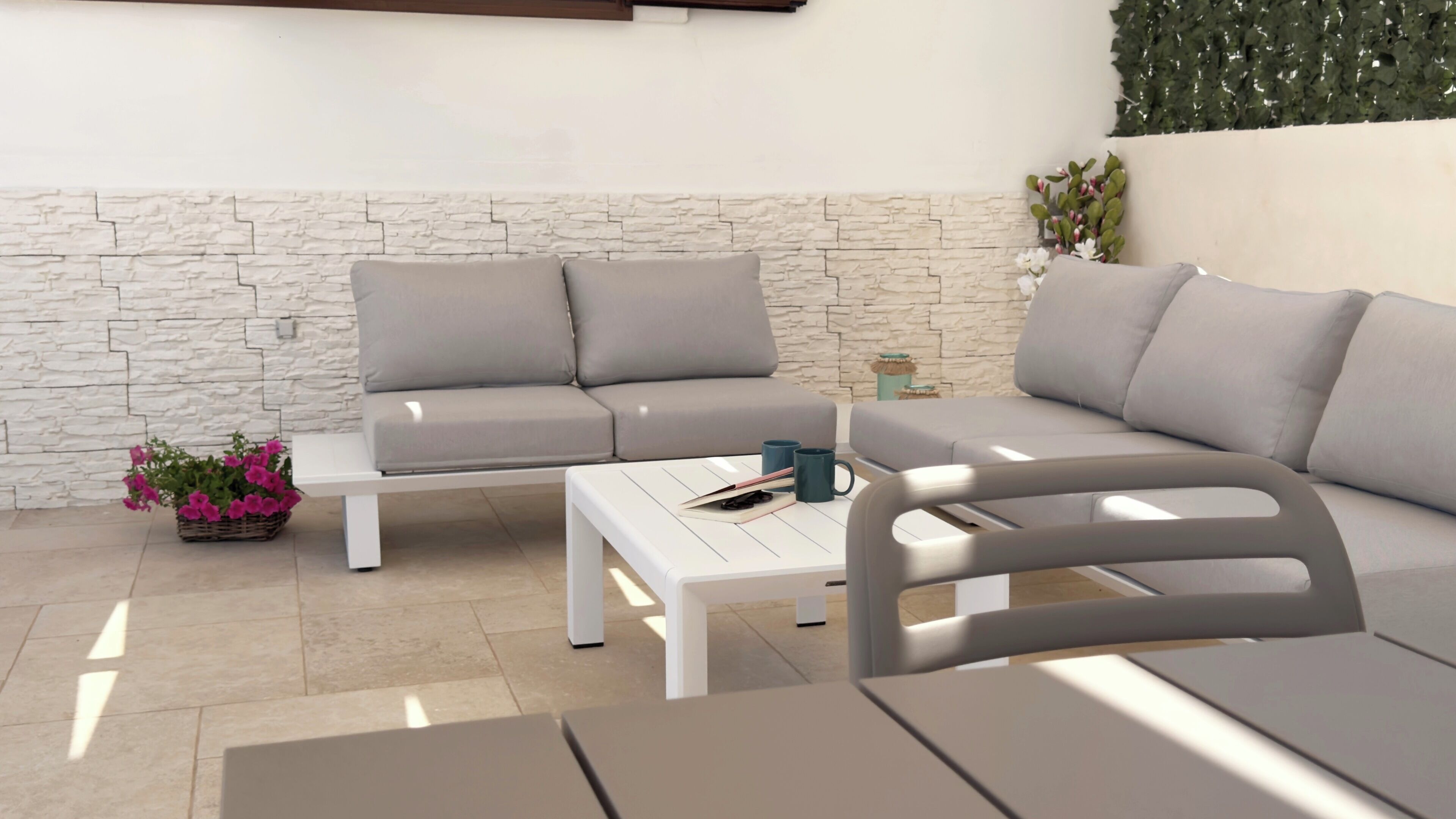 A modern outdoor seating area with a stone wall backdrop, a white coffee table, and a grey sofa.