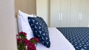 A bed with white and patterned bedding, a pillow, and a vase with pink flowers. - Alisìa (San Pietro In Bevagna)