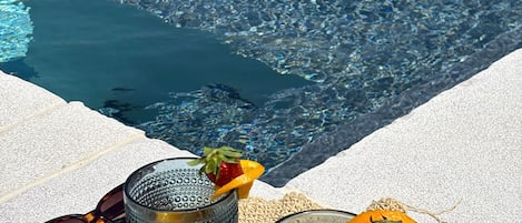 Two glasses with strawberries and an orange on a woven mat by a poolside.