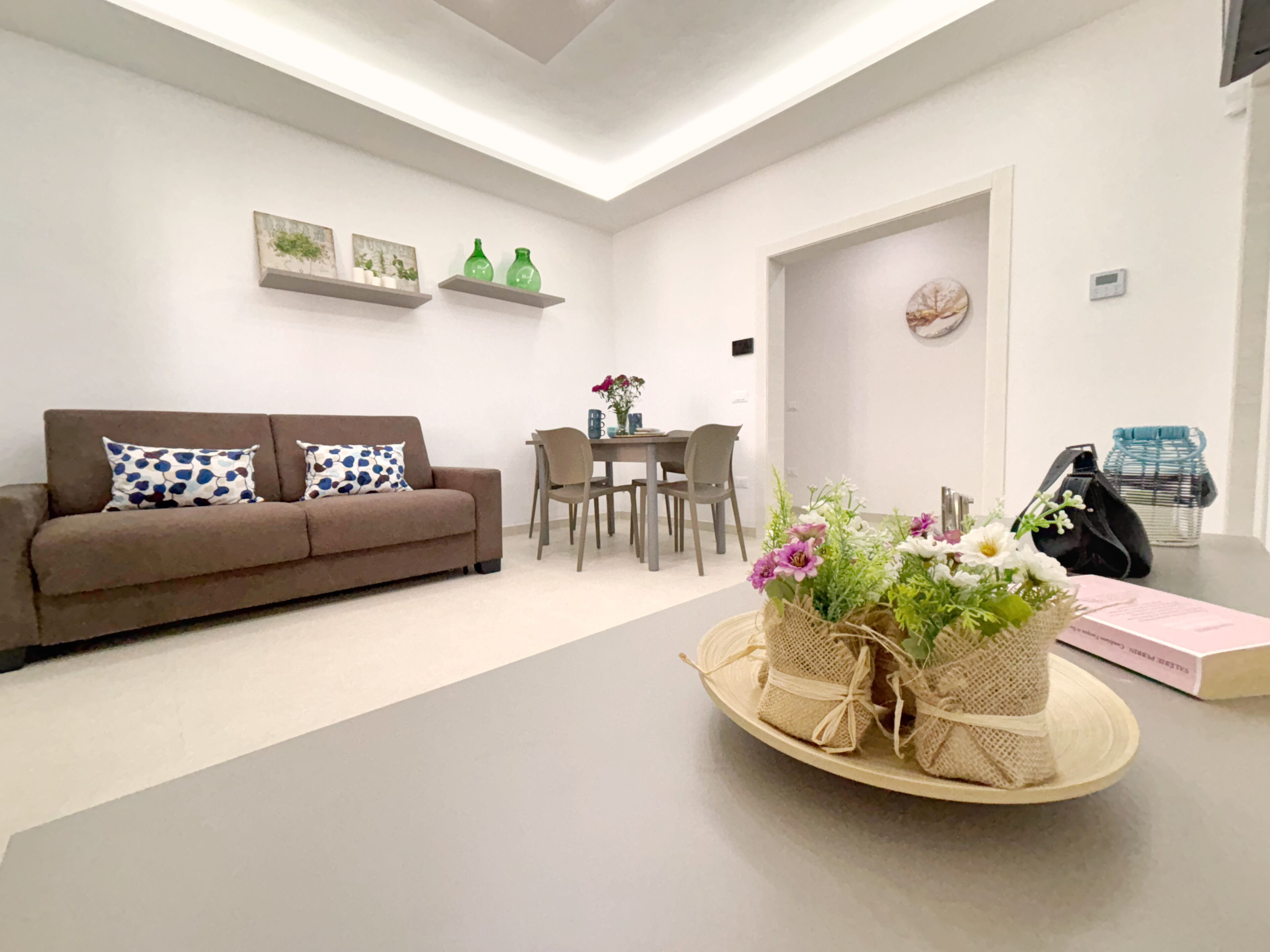 Un salon moderne avec un canapé marron, une table à manger avec des chaises, une petite plante décorative et un panier de fleurs.