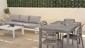 Ein moderner Außenbereich mit einer grauen Couch, einem weißen Couchtisch und einem grauen Tisch mit Stühlen.