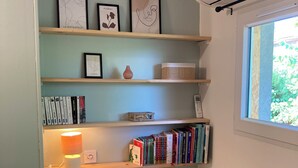 A room with a bookshelf, a lamp, a small round table, a waste bin, and a window.