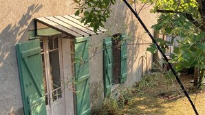 A patio with a glass table and chairs, a wooden deck, and a garden area with plants and a shed.