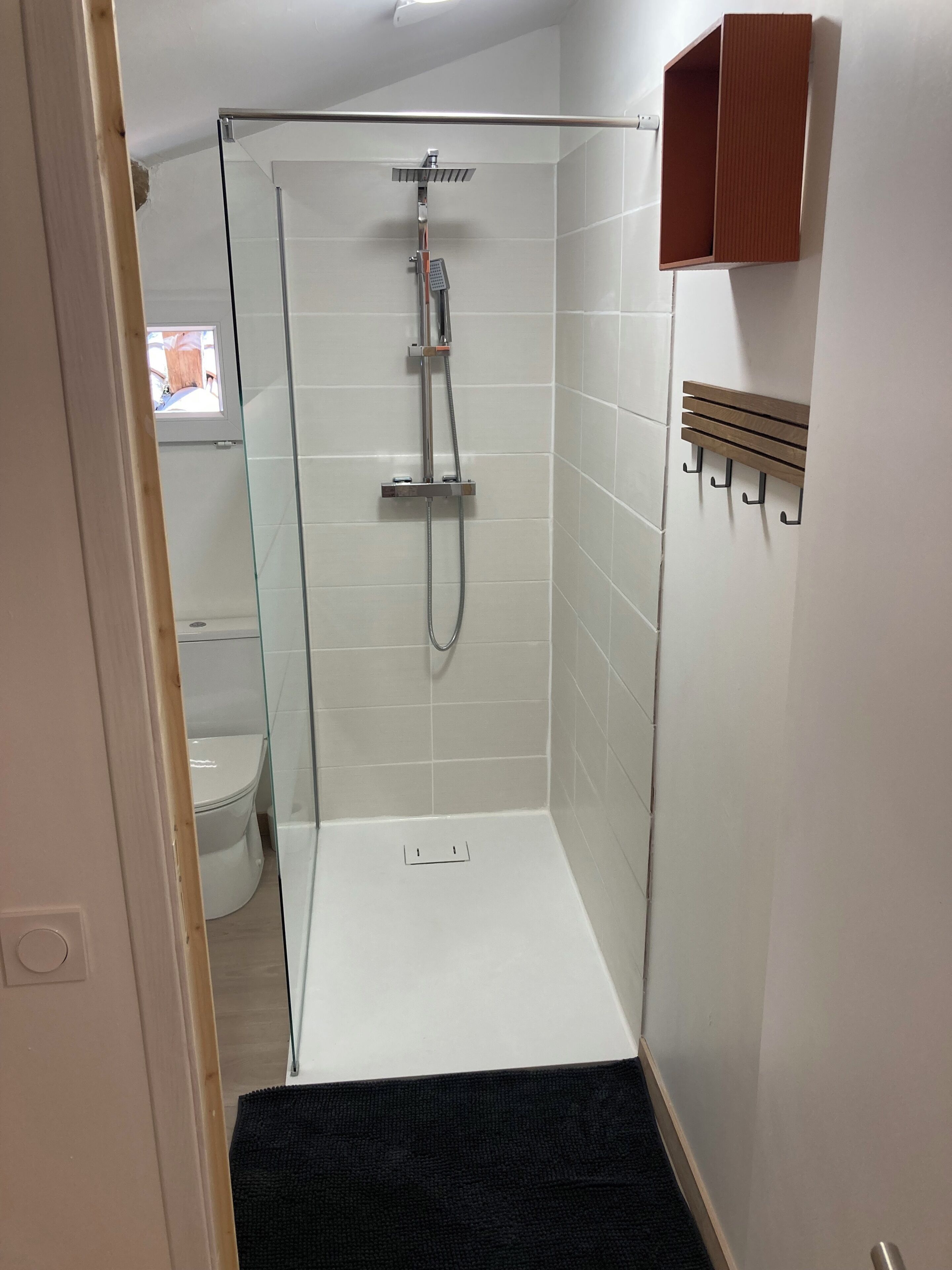 Eine Dusche mit Glastür, einer weißen Fliesenwand und einem Holzschrank.