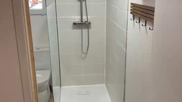 Eine Dusche mit Glastür, einer weißen Fliesenwand und einem Holzschrank.