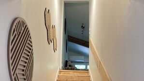 A wooden staircase leading to a room with a modern design, including a geometric wall decoration and a visible air conditioning unit.