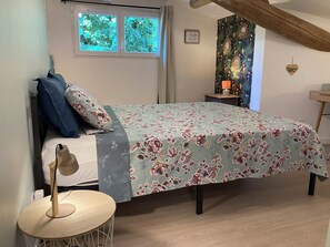 A bedroom with a bed, a bedside table, a lamp, and a window.