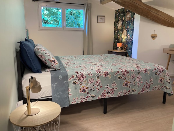 A bedroom with a bed, a bedside table, a lamp, and a window. - Lafeuillade Vacation Rental in Montech (Montech)