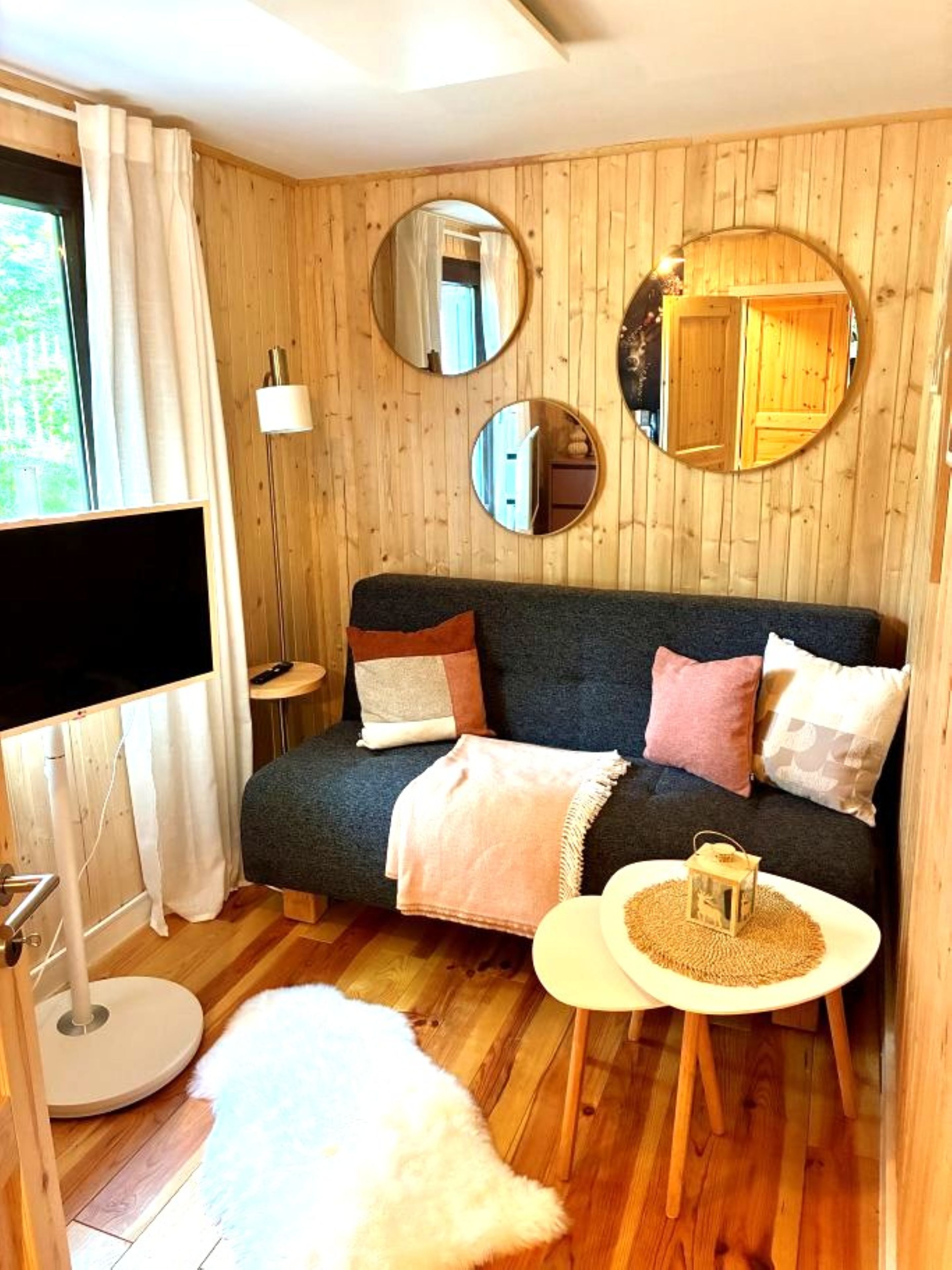 Une pièce chaleureuse avec un mur en bois, un canapé, un miroir rond, une petite table et un tapis moelleux.