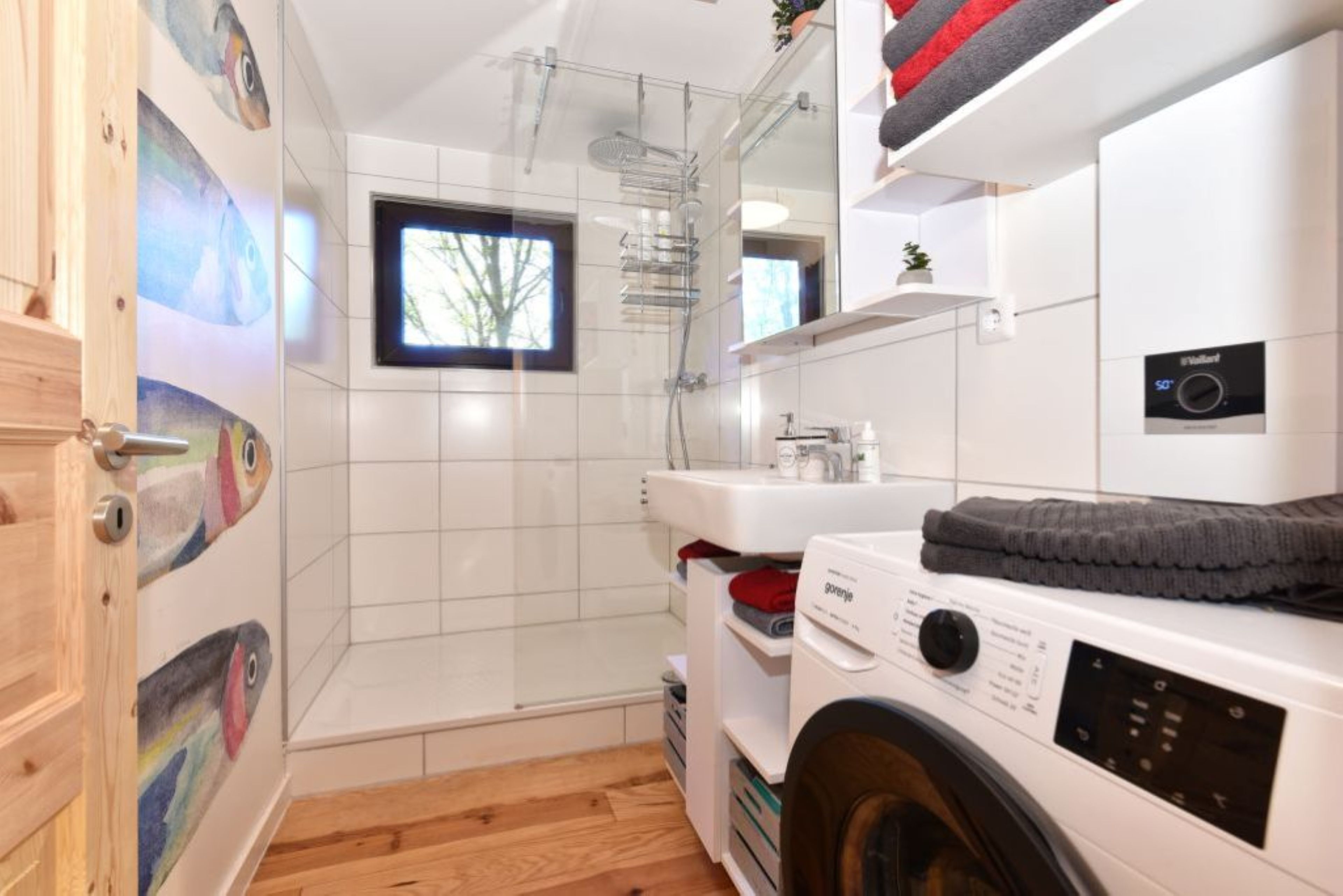 A modern bathroom with a glass shower enclosure, a washing machine, and a sink.