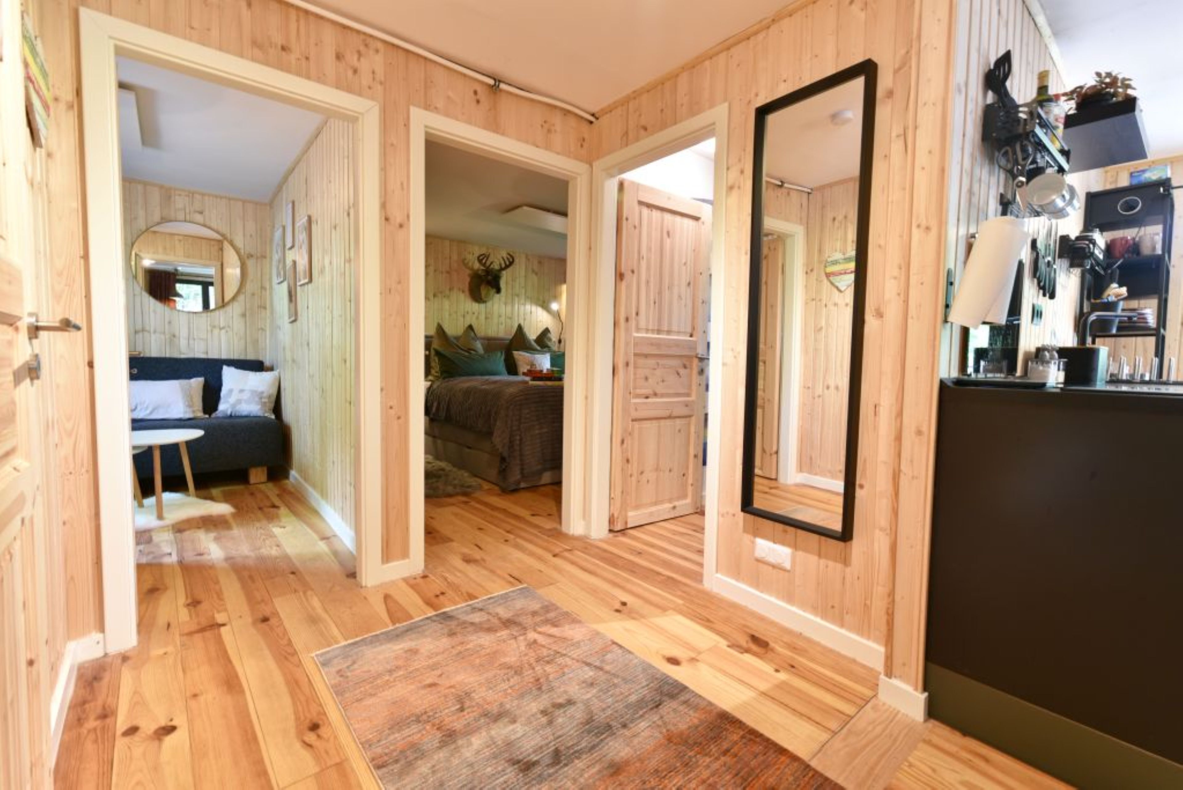 A wooden interior with a bed, a sofa, a mirror, and a kitchen area.