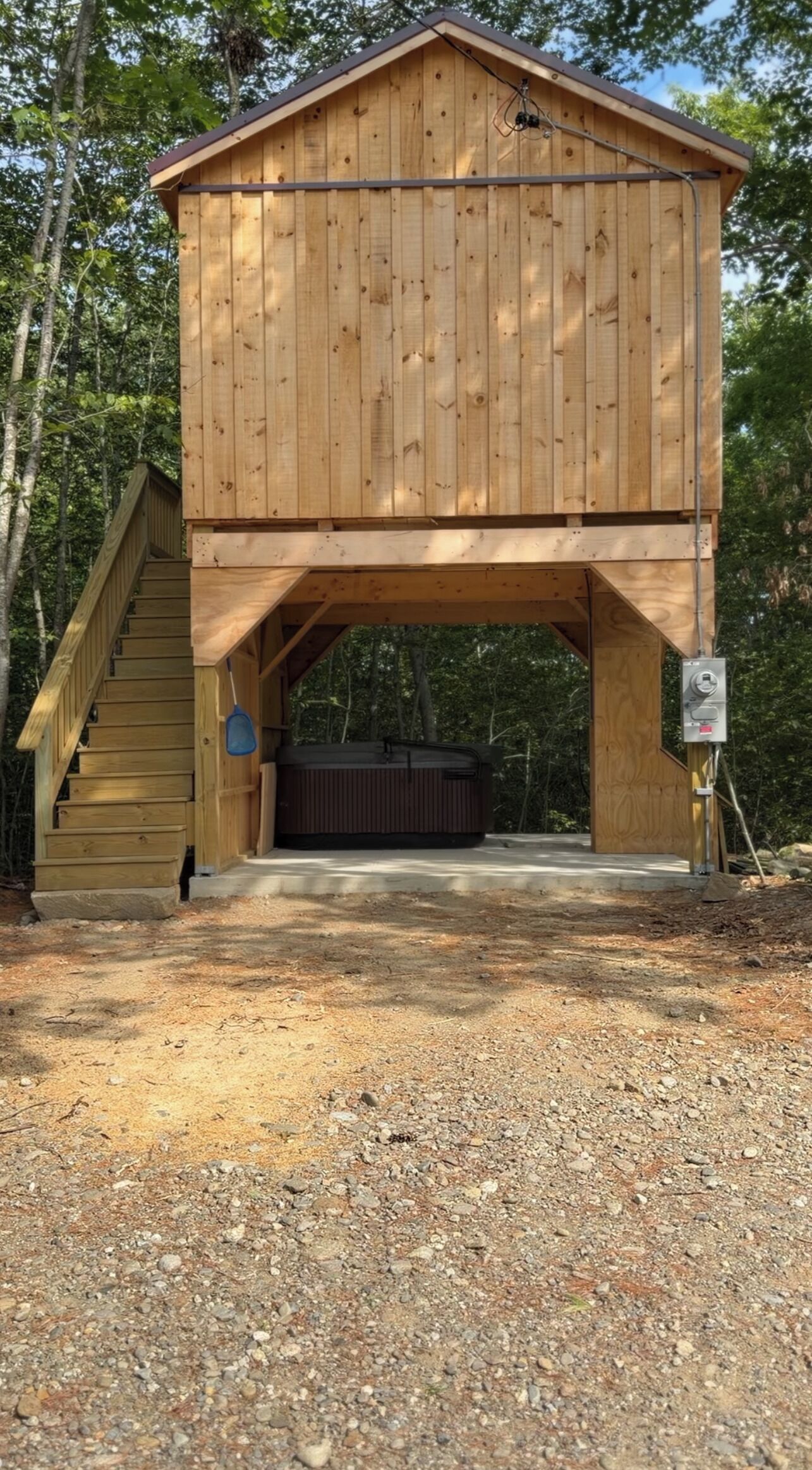A wooden structure with a staircase leading to a covered area, surrounded by trees.