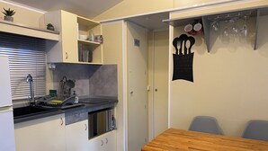 A compact kitchen with a sink, cabinets, and a dining area with a table and chairs. - Mobile home near the ocean with a pool (Le Pradet)