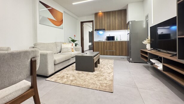A modern living room with a sofa, coffee table, TV, and kitchen area in the background. - Stunning 1-Bdr Apart With Pool, Gym, Restaurant (Kinshasa)