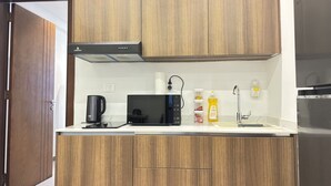 A compact kitchen with wooden cabinets, a microwave, a coffee maker, and a sink. - Stunning 1-Bdr Apart With Pool, Gym, Restaurant (Kinshasa)