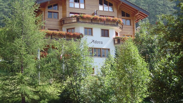 A multi-story wooden building with balconies, surrounded by trees and mountains. - Adora Leukerbad # 4-bed apartment, Bad, WC by Interhome (Leukerbad)