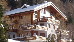 A multi-story hotel with balconies, wooden exterior, and snow-covered surroundings. - Adora Leukerbad # 4-bed apartment, Bad, WC by Interhome (Leukerbad)