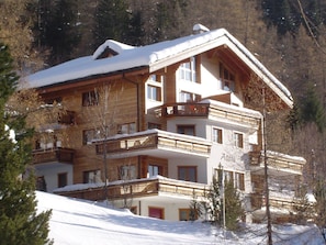 Ein mehrstöckiges Hotel mit Balkonen, Holzfassade und verschneiter Umgebung.
