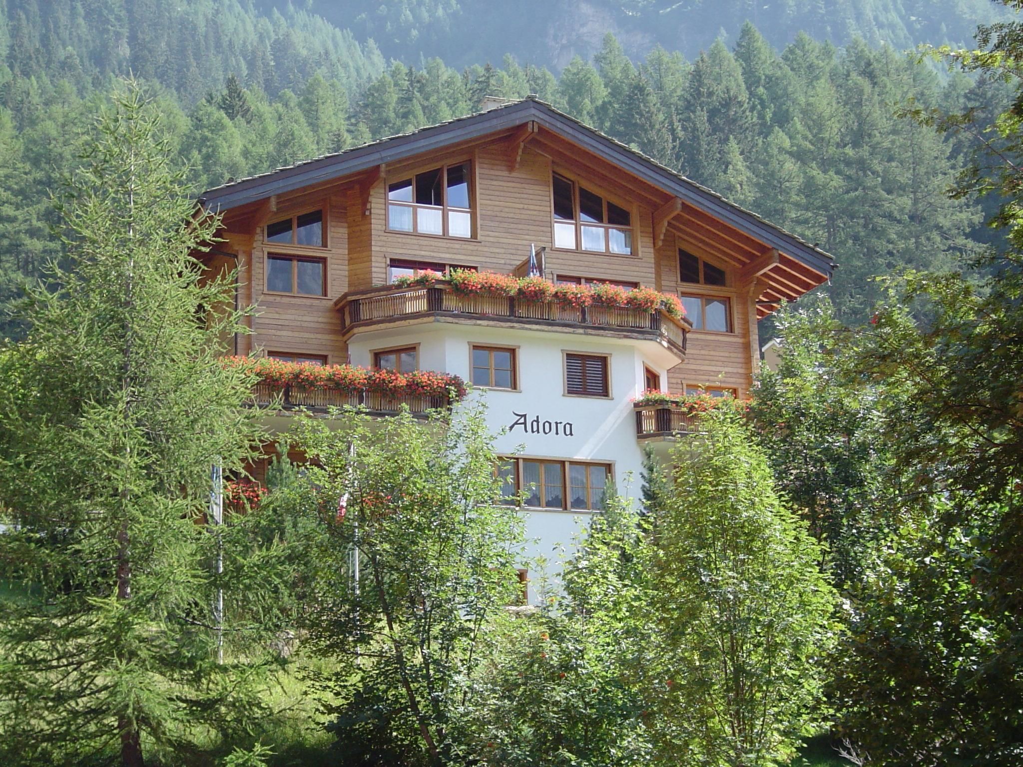 Ein mehrstöckiges Holzhaus mit Balkonen, umgeben von Bäumen und Bergen.