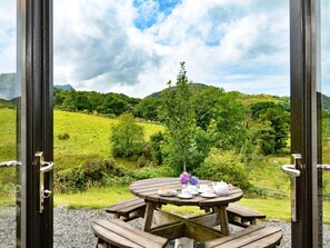 Ein Holztisch für ein Picknick mit Blick auf eine grüne Landschaft durch offene Türen.