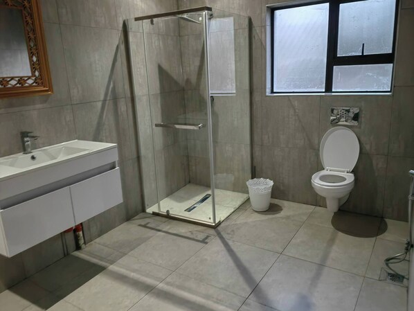 Een badkamer met een douchecabine van glas, een wastafel, toilet en een raam.
