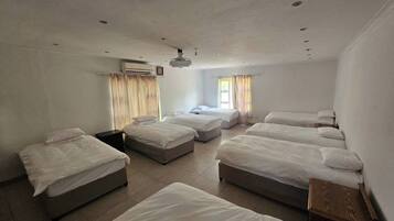 A hotel room with four beds, a ceiling fan, an air conditioning unit, and a window with curtains.