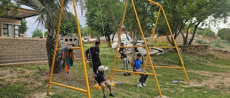 A playground with yellow swings and a brick wall in the background.