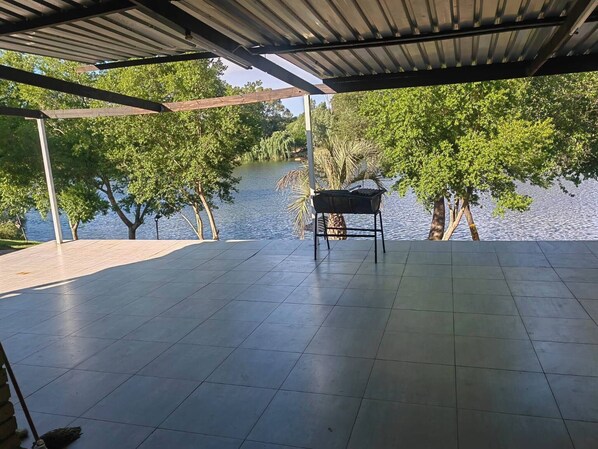 A covered patio with a grill, a tiled floor, and a view of a lake with trees.