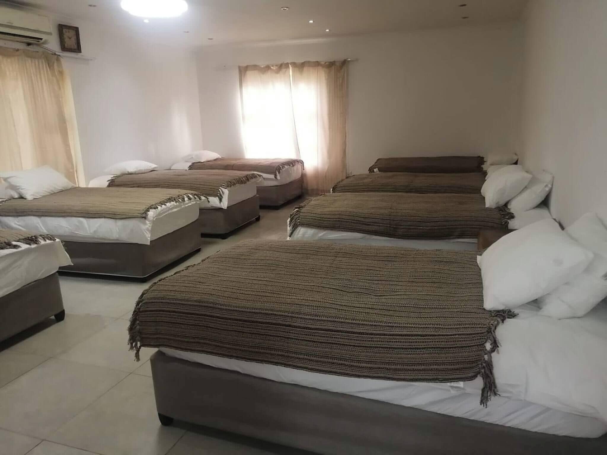 A hotel room with four beds arranged in a row, a large window with curtains, and a ceiling light.