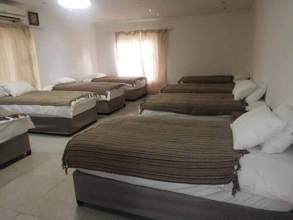A hotel room with four beds arranged in a row, a large window with curtains, and a ceiling light.