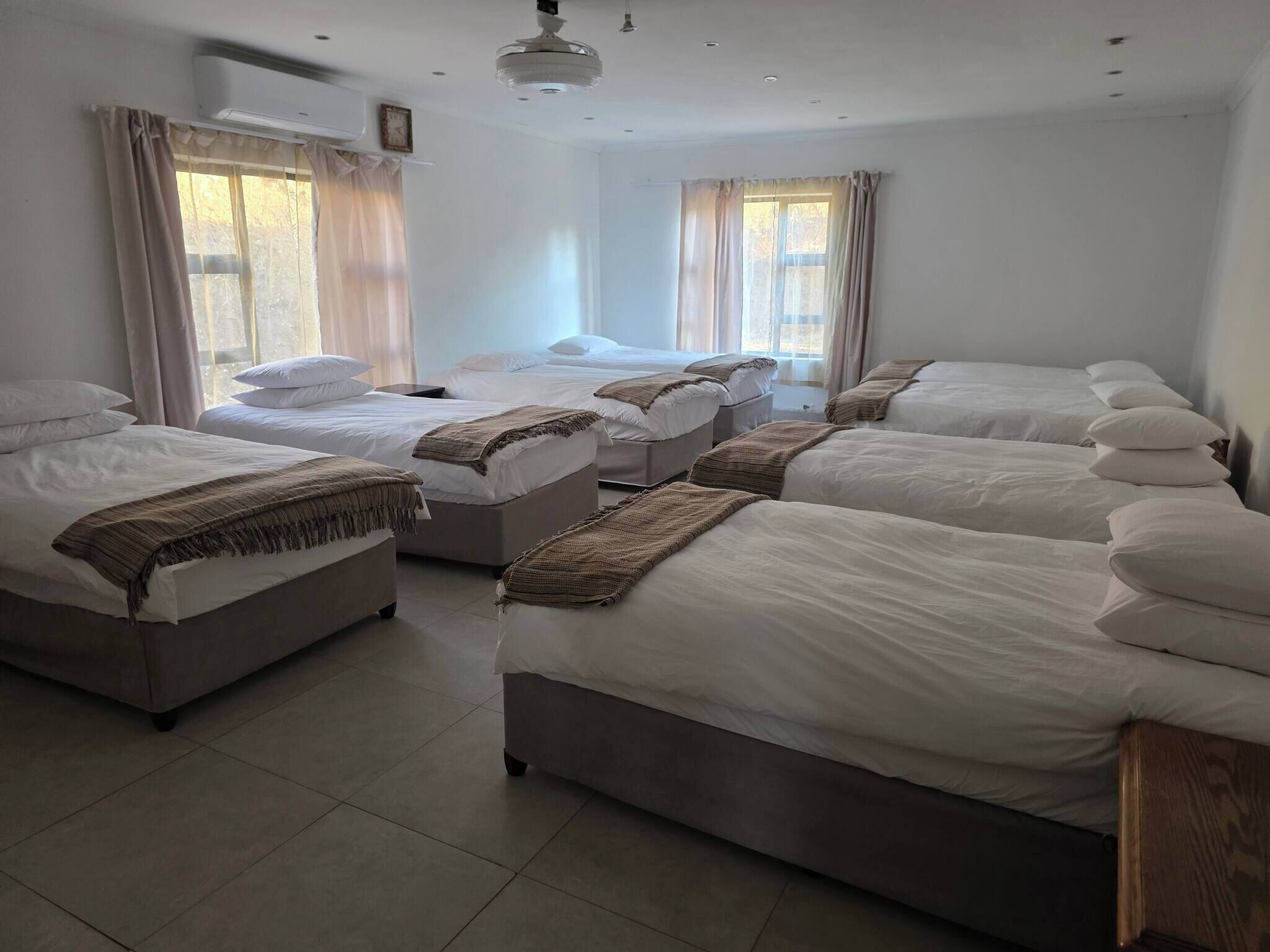 A hotel room with multiple beds, a ceiling fan, and large windows with curtains.