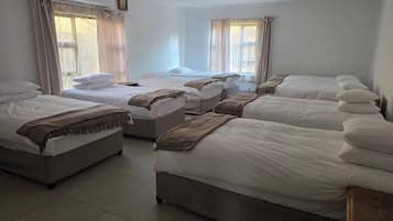 A hotel room with multiple beds, a ceiling fan, and large windows with curtains.