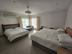 Une chambre d’hôtel avec deux lits, un canapé, un fauteuil et un ventilateur de plafond.